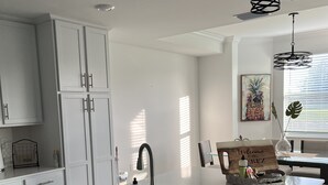 Une cuisine moderne avec des meubles blancs, un évier en acier inoxydable et un luminaire suspendu noir.