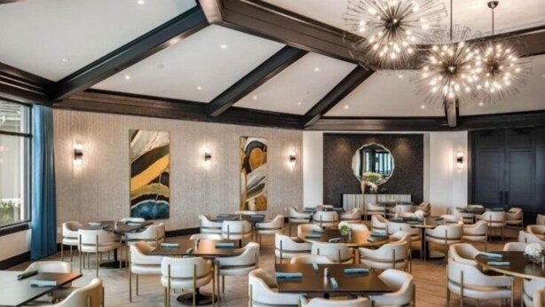 Un vaste espace dédié à la salle à manger, avec plusieurs tables et chaises, un lustre moderne et un grand miroir au mur.
