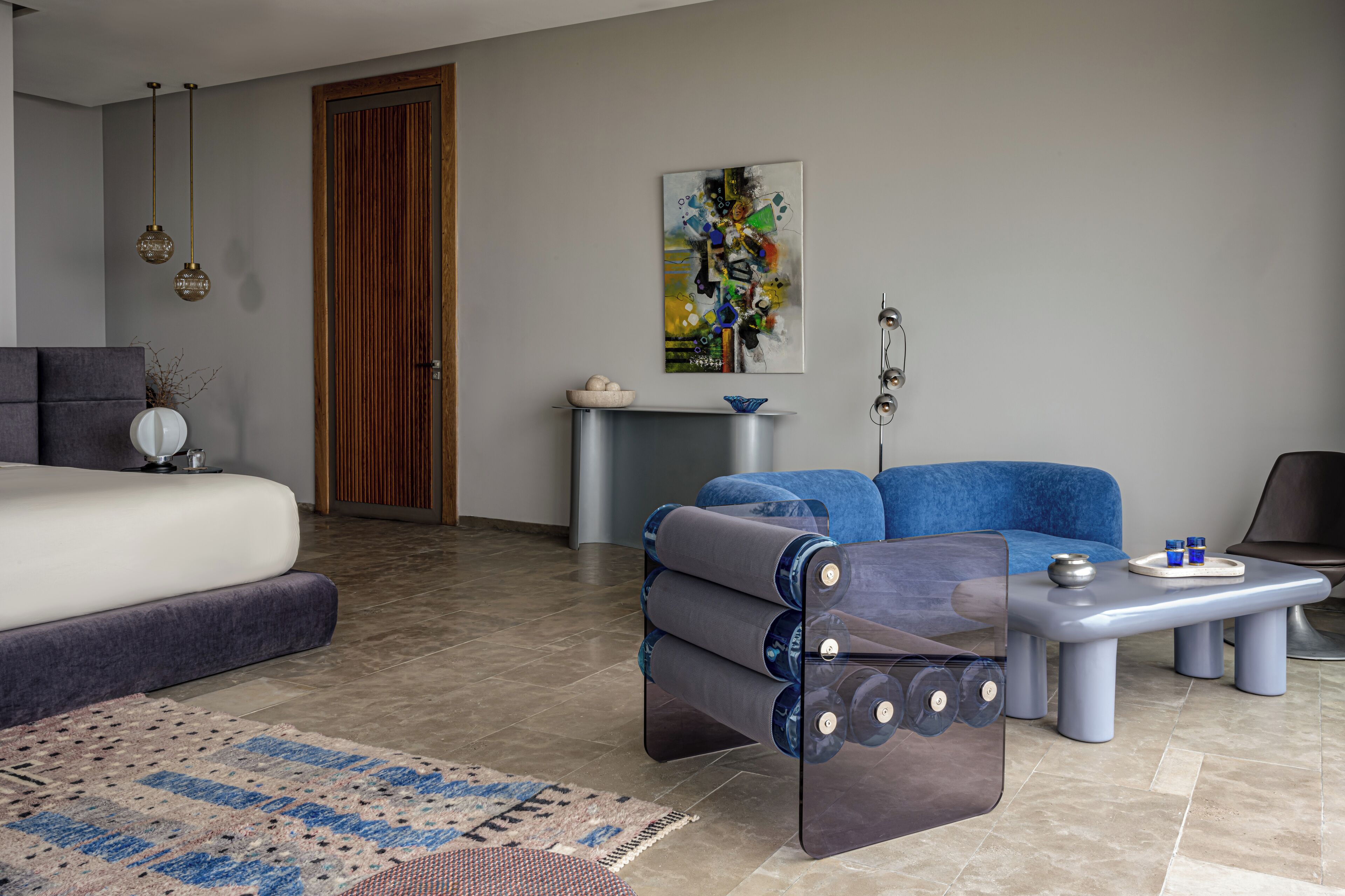 A modern living room with a sofa, a coffee table, and a dining table. There is a painting on the wall and a door in the background.