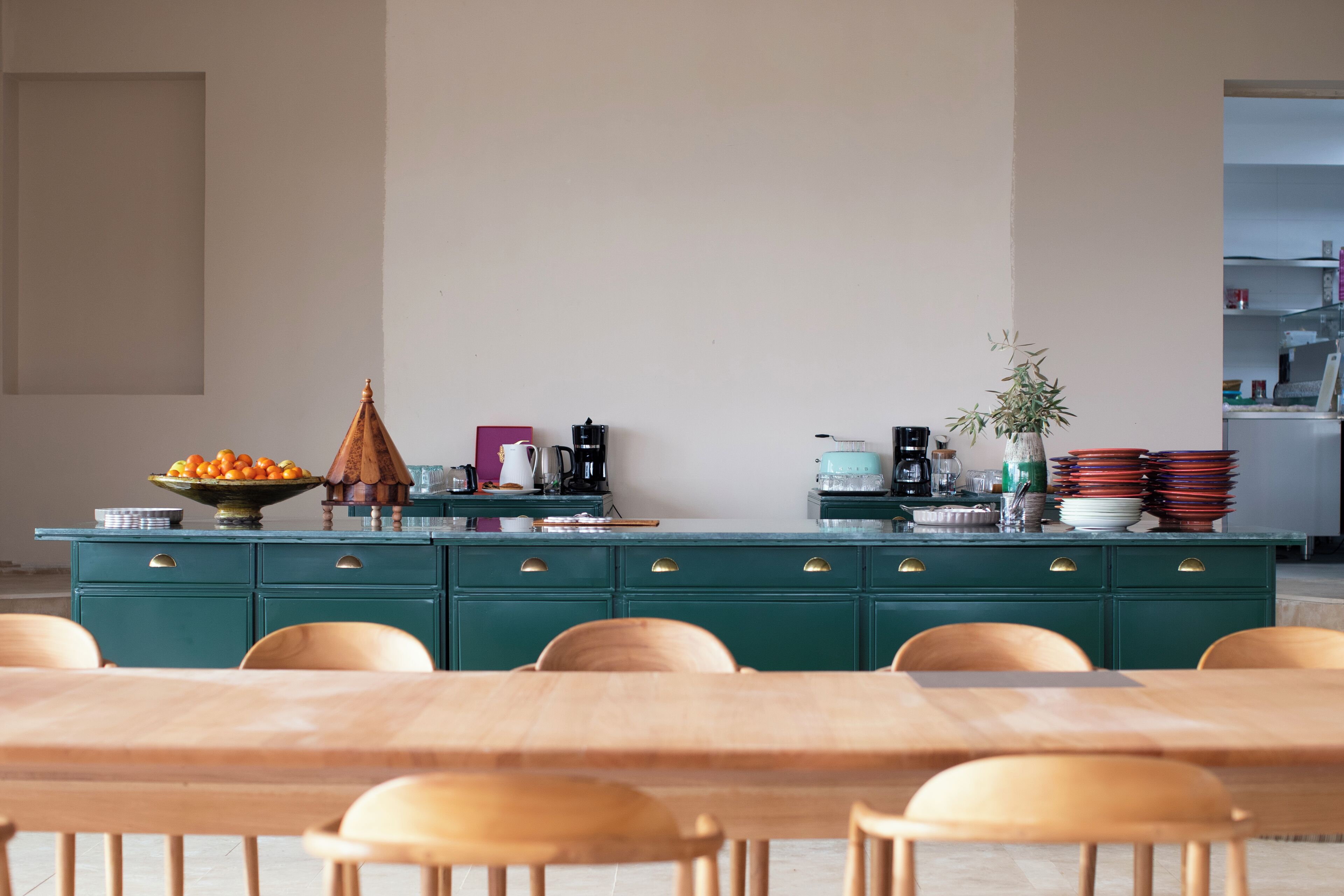 Un comedor con una mesa y sillas de madera, un armario verde con electrodomésticos de cocina y un cuenco de fruta sobre la encimera.