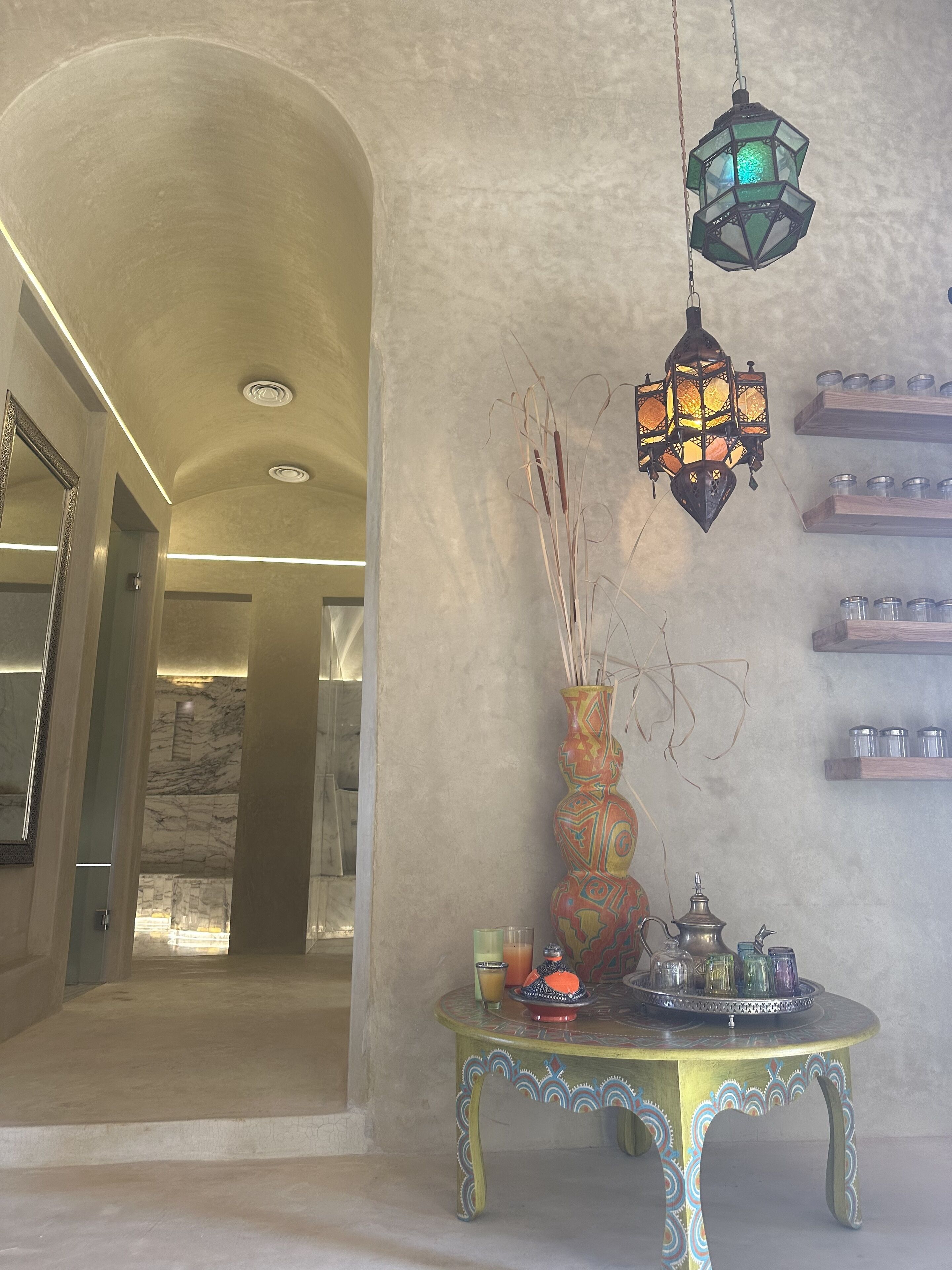 A hallway with a decorative table, a hanging lantern, and a marble wall.