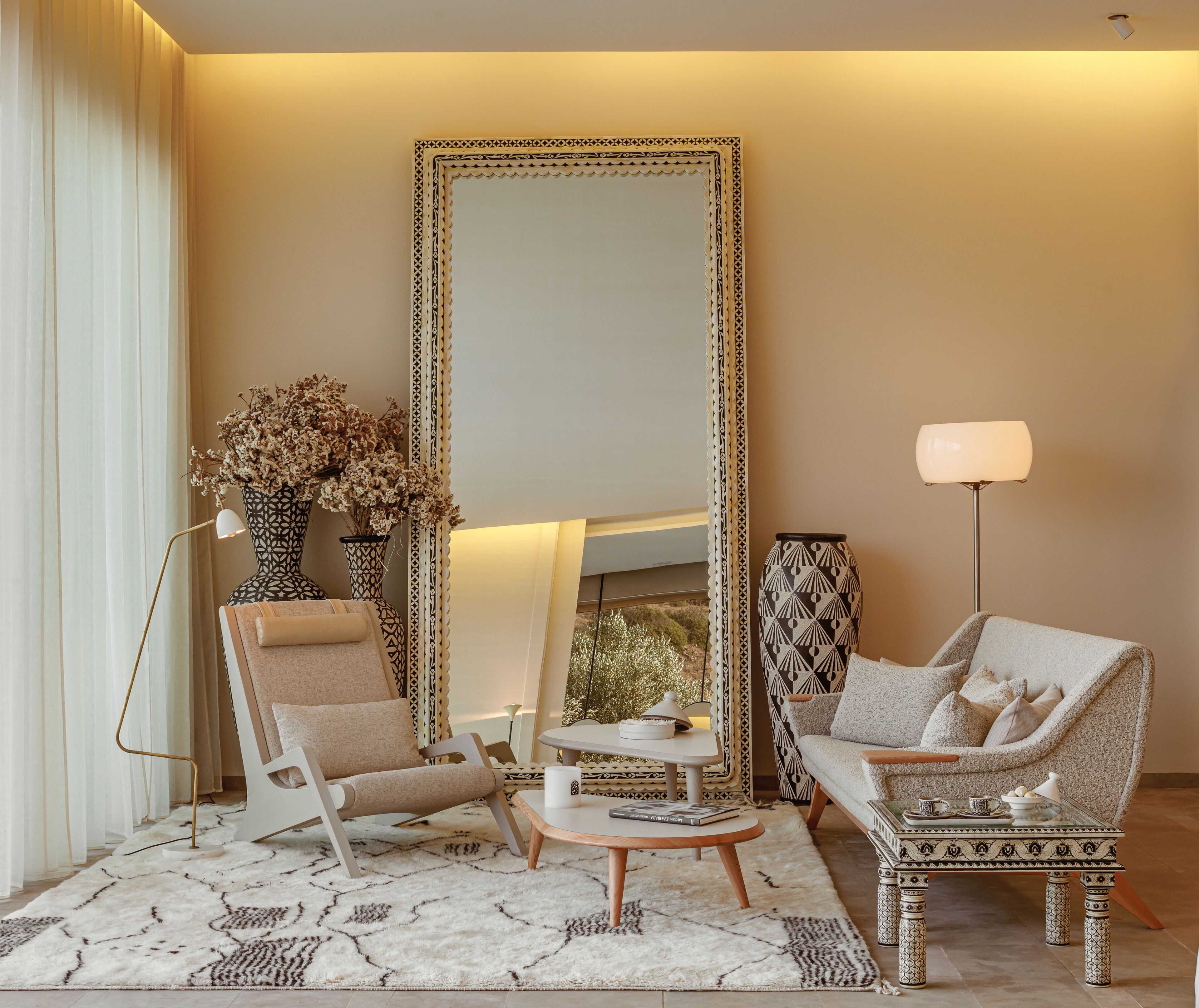 A modern living room with a large mirror, two armchairs, a coffee table, and decorative vases.