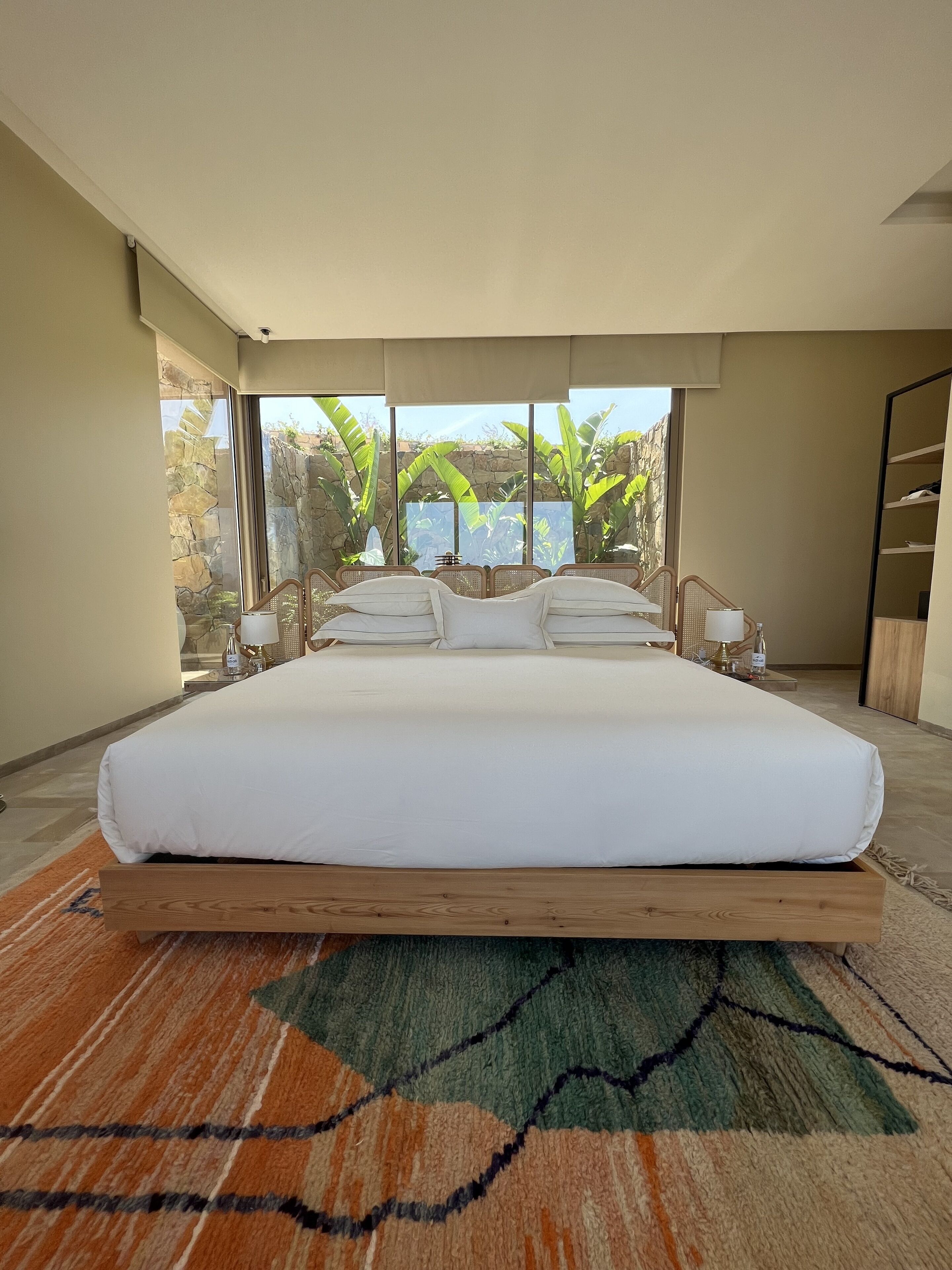Un dormitorio moderno con una cama grande, vistas a zonas verdes y una pared de piedra.