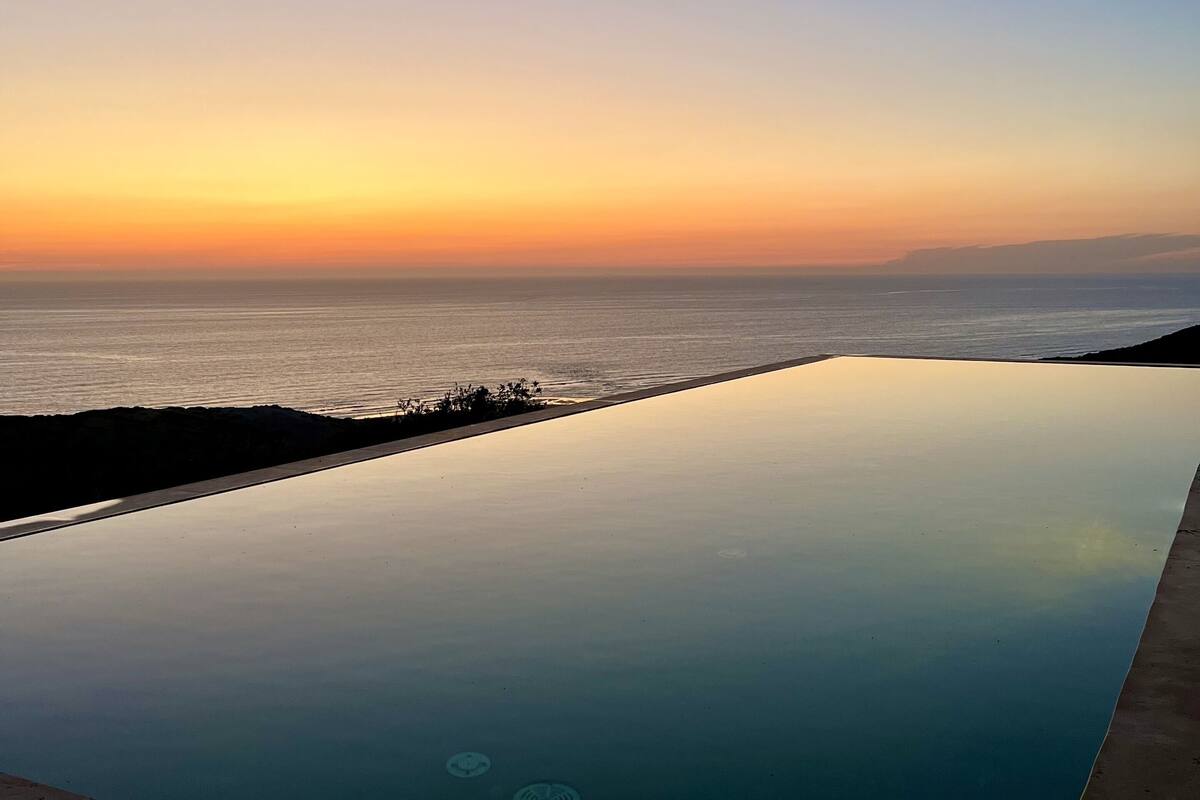 Une piscine à débordement offrant une vue sur l’océan au coucher du soleil.