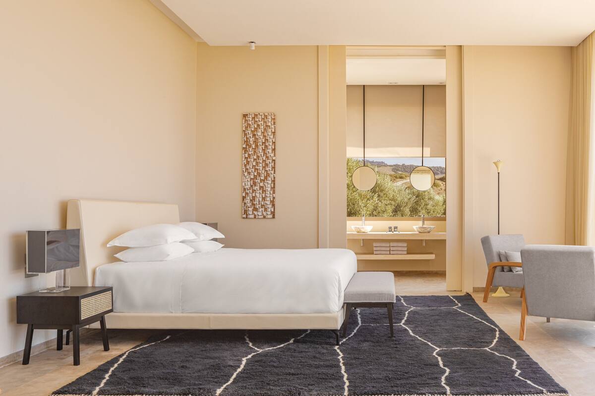 Une chambre d’hôtel moderne équipée d’un lit, d’une table de chevet, d’une chaise et offrant une vue sur l’extérieur.