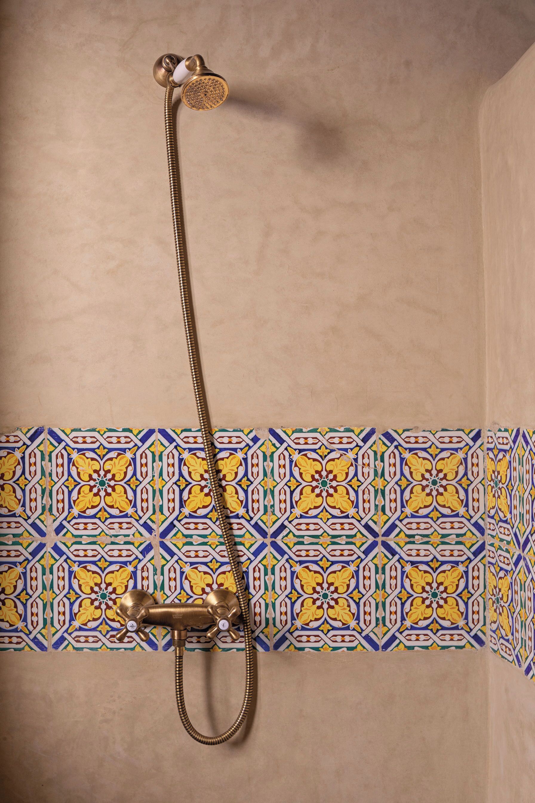 Een douche met een messing armatuur en een betegelde rand.