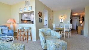 A living room with a sofa, chairs, a coffee table, a dining table with chairs, a kitchen area, and a hallway. - AMAZING OCEANFRONT CONDO - 809 Brandywine House, Sea Colony, Bethany Beach (Bethany Beach)