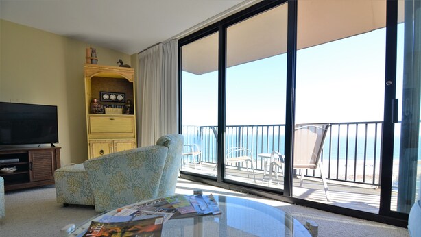 A hotel room with a balcony, a television, a sofa, and a glass table with magazines. - AMAZING OCEANFRONT CONDO - 809 Brandywine House, Sea Colony, Bethany Beach (Bethany Beach)