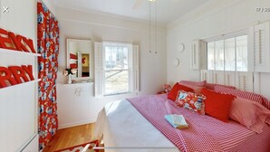 Un dormitorio con una cama grande, una ventana con persianas, un espejo y una colcha a cuadros rojos y blancos.