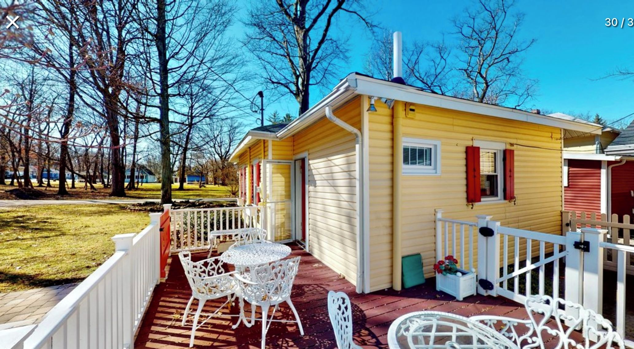 A yellow cabin with a porch, white railing, and outdoor seating.