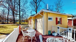 A yellow cabin with a porch, white railing, and outdoor seating. - Cheeky Cherry Cottage (Lakeside Marblehead)