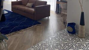Ein Wohnzimmer mit einem braunen Sofa, einem blauen Teppich und fußbodenhohen, gemusterten Fliesen.