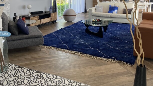 Ein modernes Wohnzimmer mit großem Fernseher, einer Couch, einem Couchtisch und einem blauen Teppich.