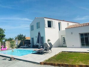 Une maison moderne dotée d’une piscine, d’un patio avec des chaises longues et d’un petit jardin.
