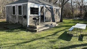A small, single-story cabin with a porch and a grill outside. - Adorable Cape Cottage Near Kingsbury Beach (Eastham)