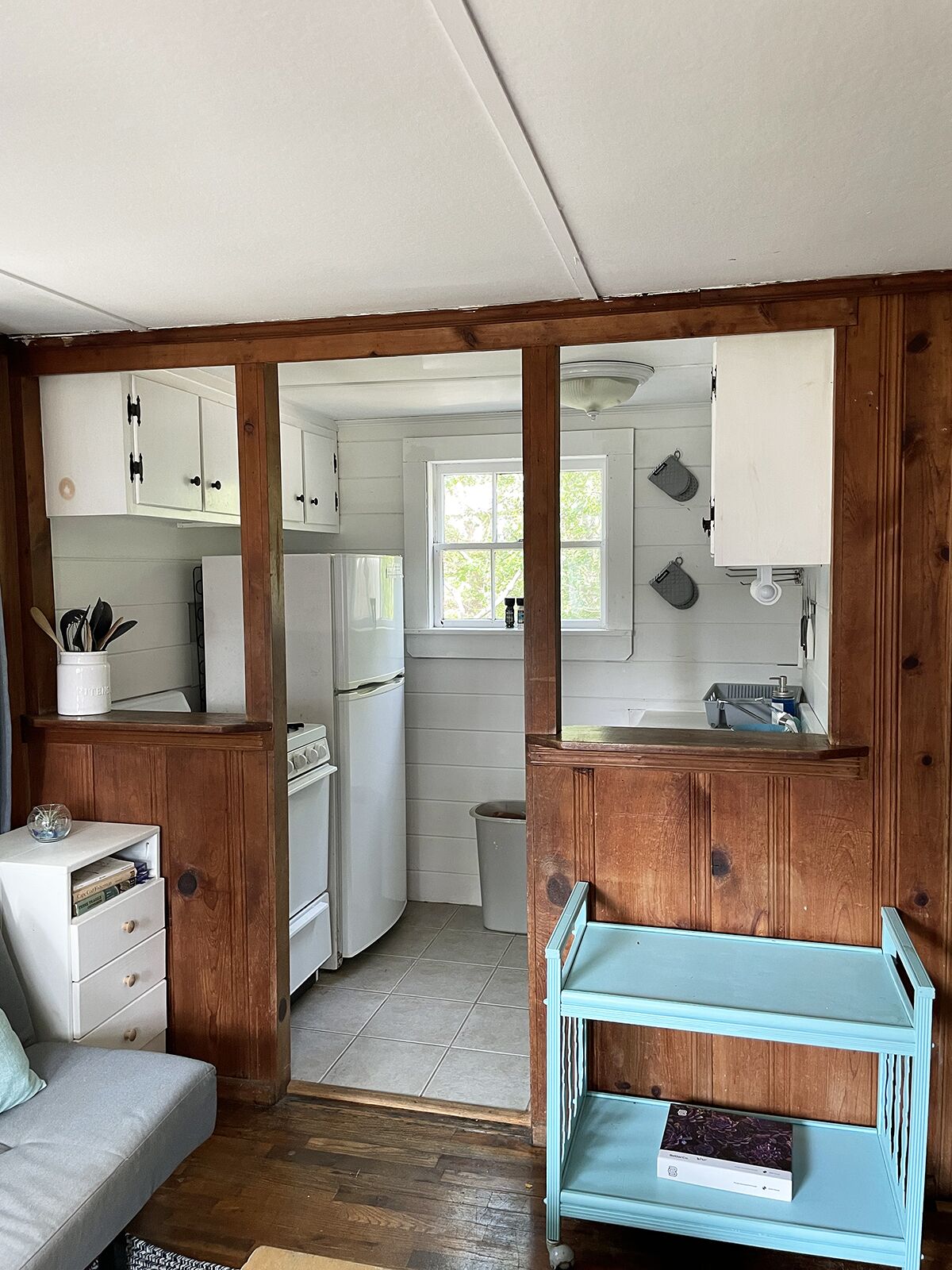Une cuisine compacte avec des meubles de rangement en bois, un réfrigérateur blanc, un évier et un chariot de rangement bleu.