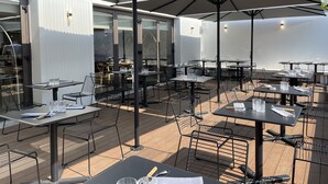 An outdoor dining area with tables and chairs under large umbrellas, surrounded by a white wall and glass windows. - Le Vert Bocage (Franqueville-Saint-Pierre)