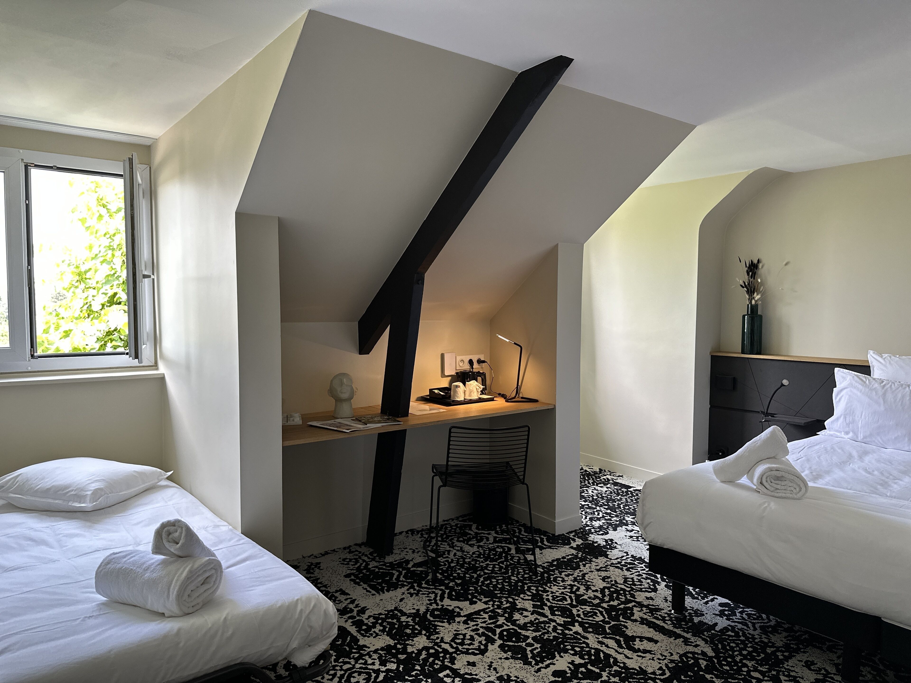Een slaapkamer met twee bedden, een bureau, een stoel, een lamp en een raam met daglicht.