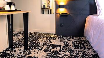 Une chambre d’hôtel avec un lit, une table de chevet, un miroir et une moquette à motifs.