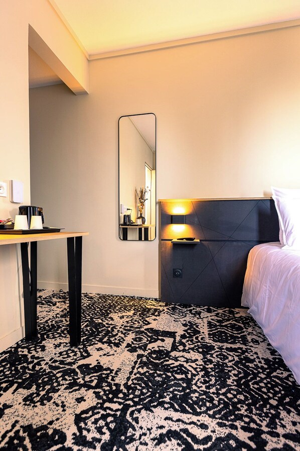 Una habitación de hotel con una cama, una mesita de noche, un espejo y una alfombra estampada.
