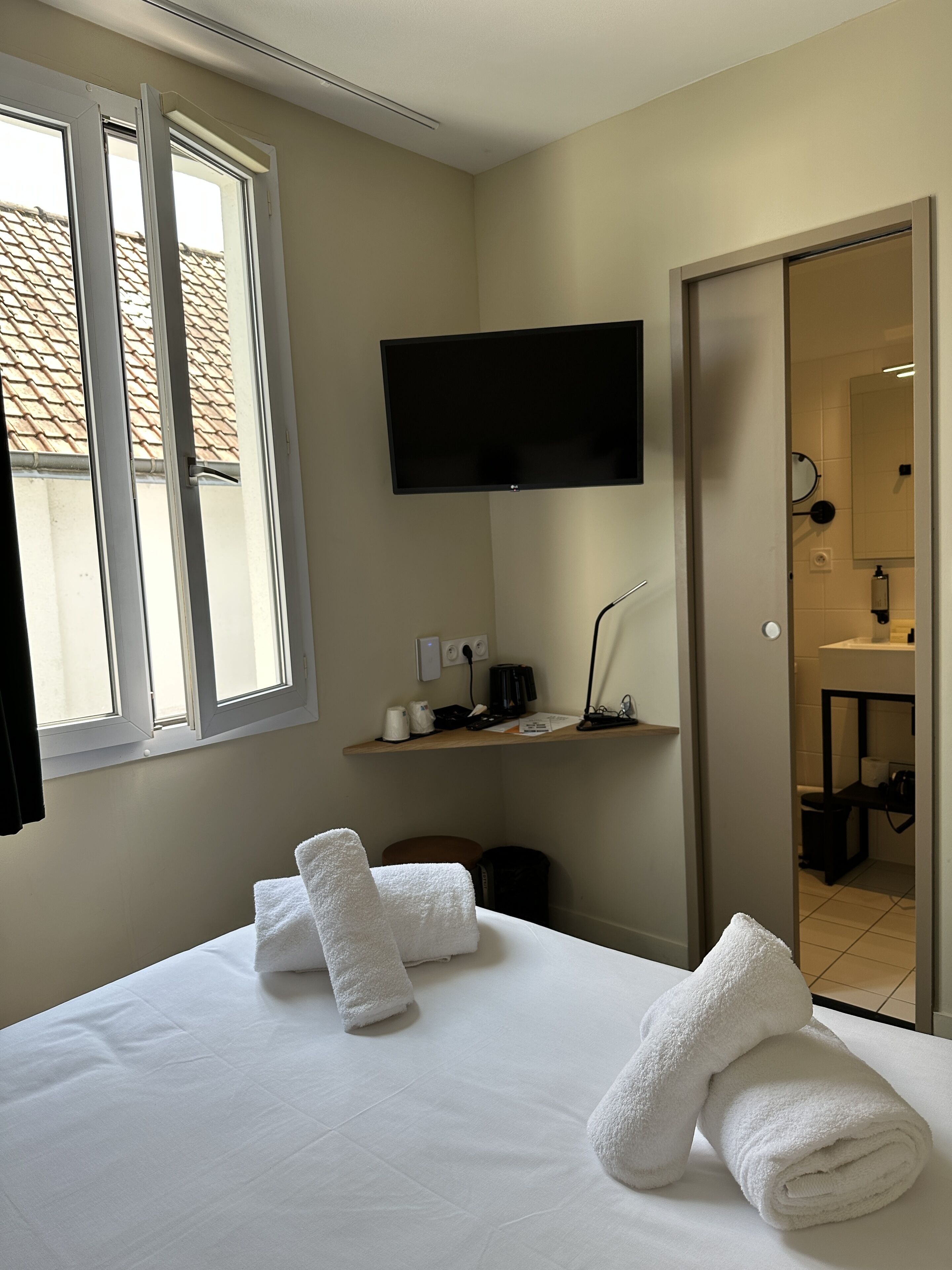 Camera d'albergo con un letto, una TV a schermo piatto montata a parete, una scrivania con una lampada e vista all'esterno da una finestra.