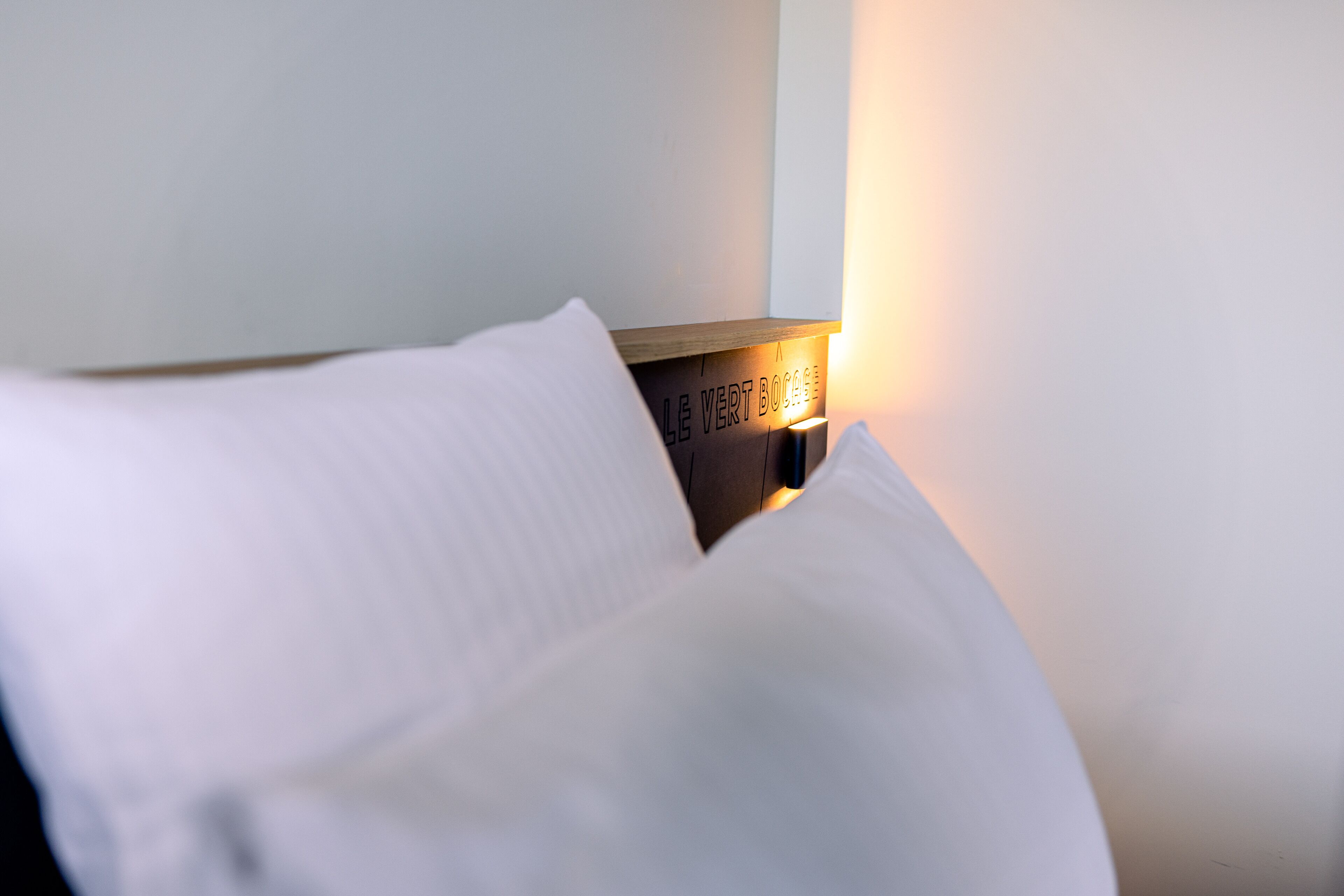 Una cama bien hecha con un cojín y una mesita de noche con una lámpara.