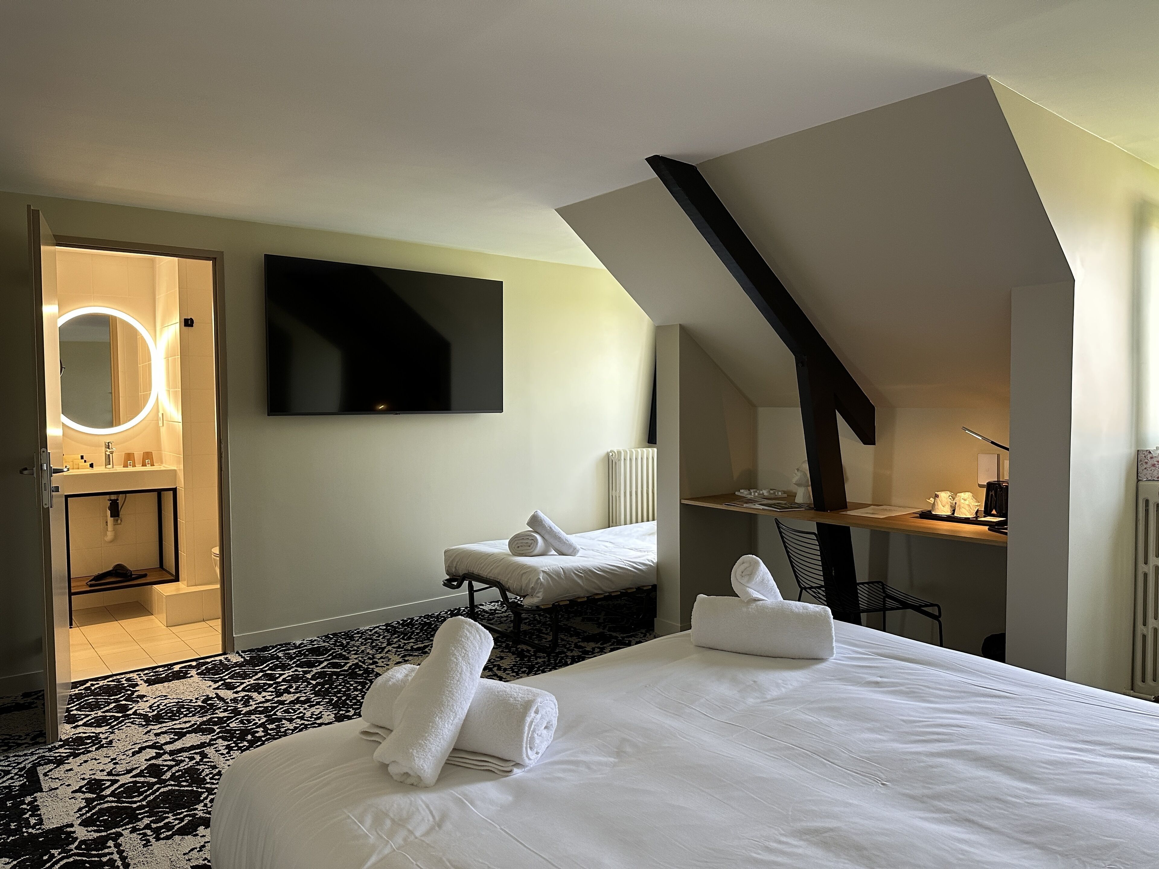 Een moderne hotelkamer met een groot bed, een zithoek met een fauteuil, een bureau en een aan de muur bevestigde televisie.
