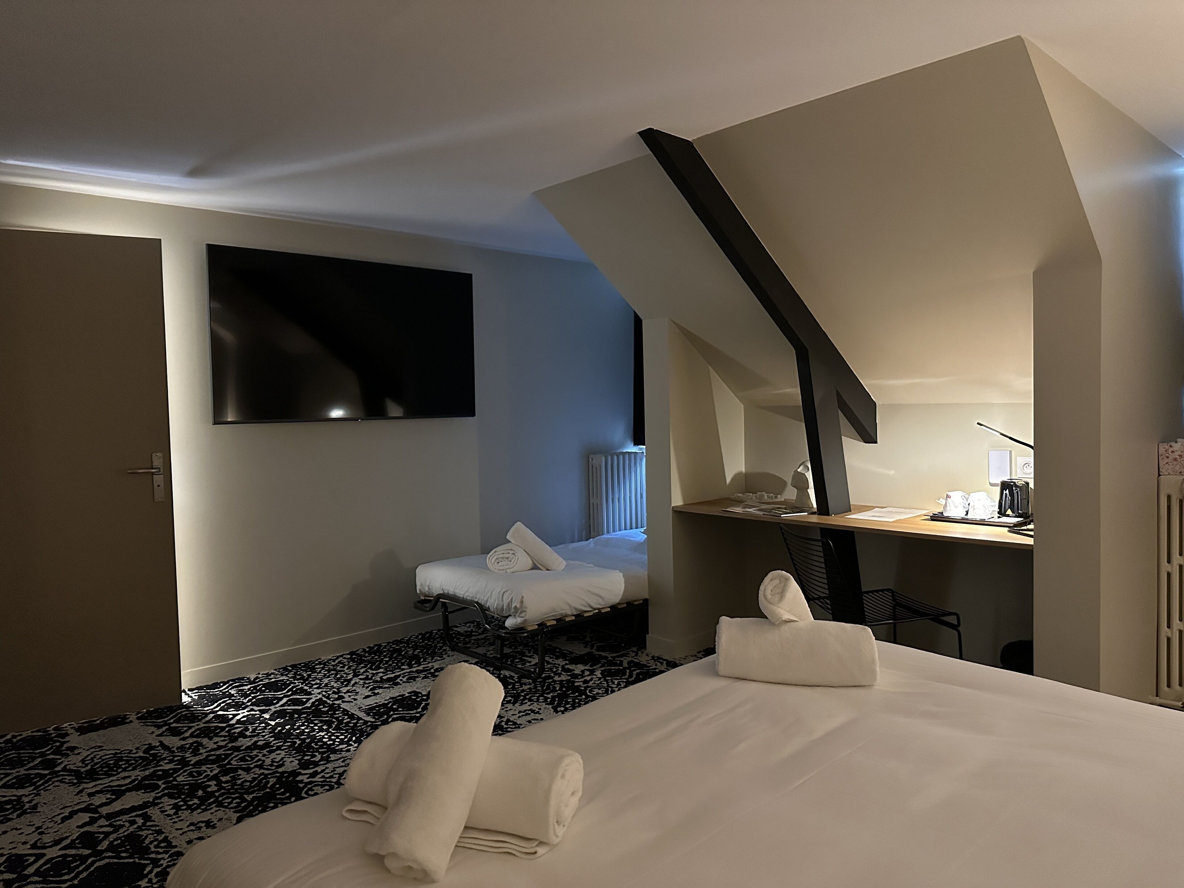 Habitación de hotel con cama, escritorio, silla, televisión y radiador.