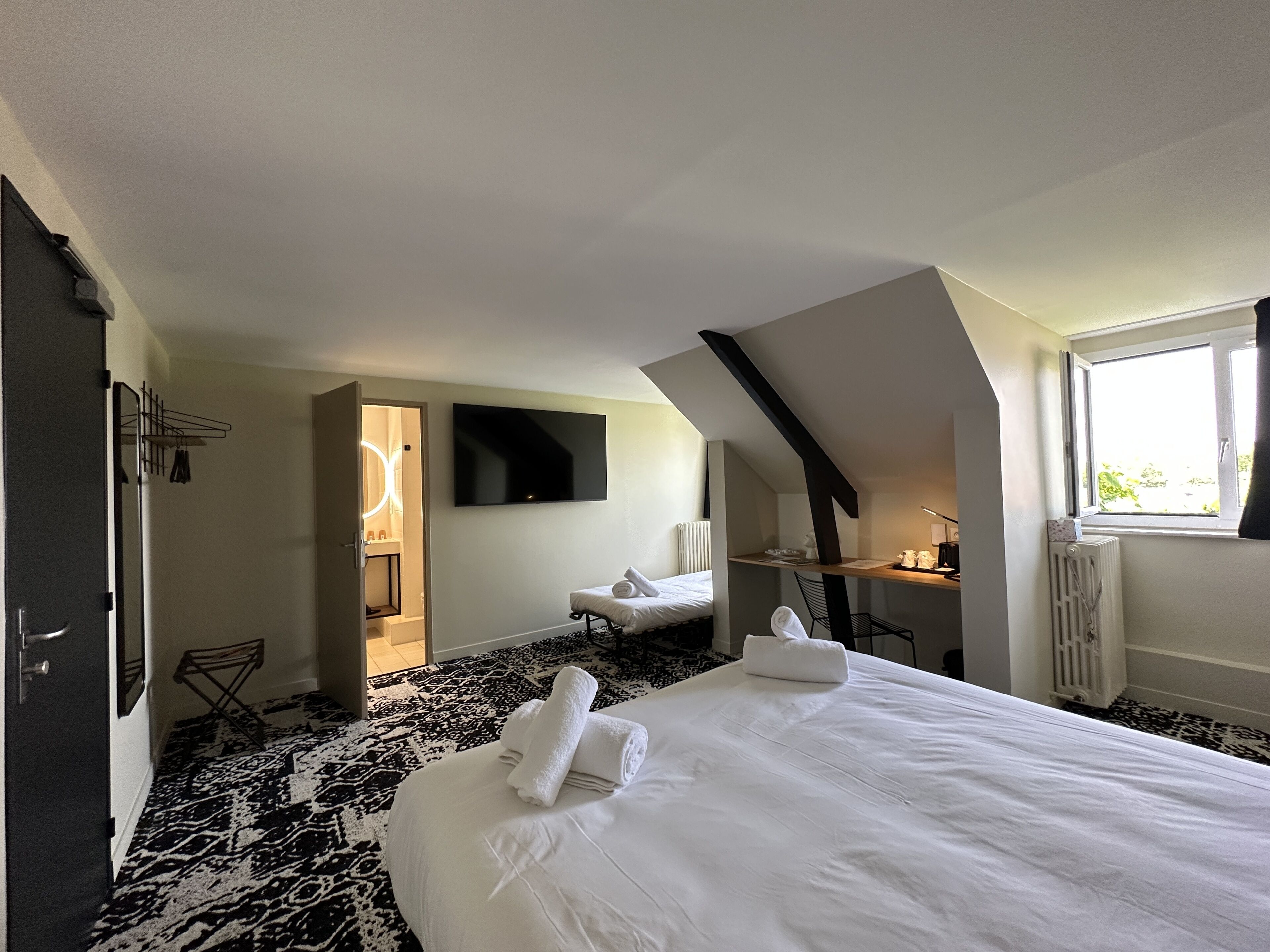 Een hotelkamer met een bed, bureau, stoel, televisie en raam.