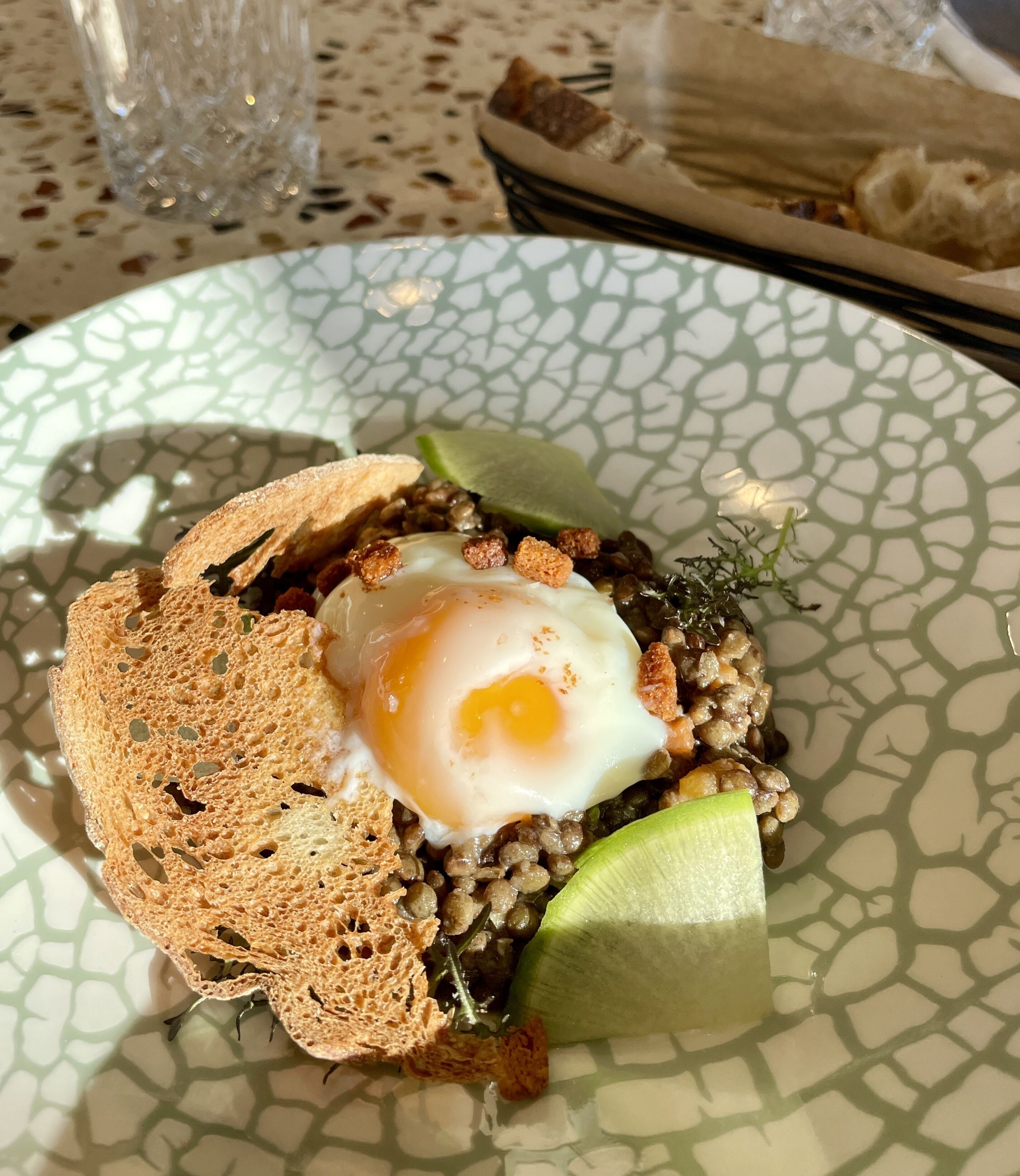 A plate with a poached egg, lentils, and a slice of bread on a patterned plate.