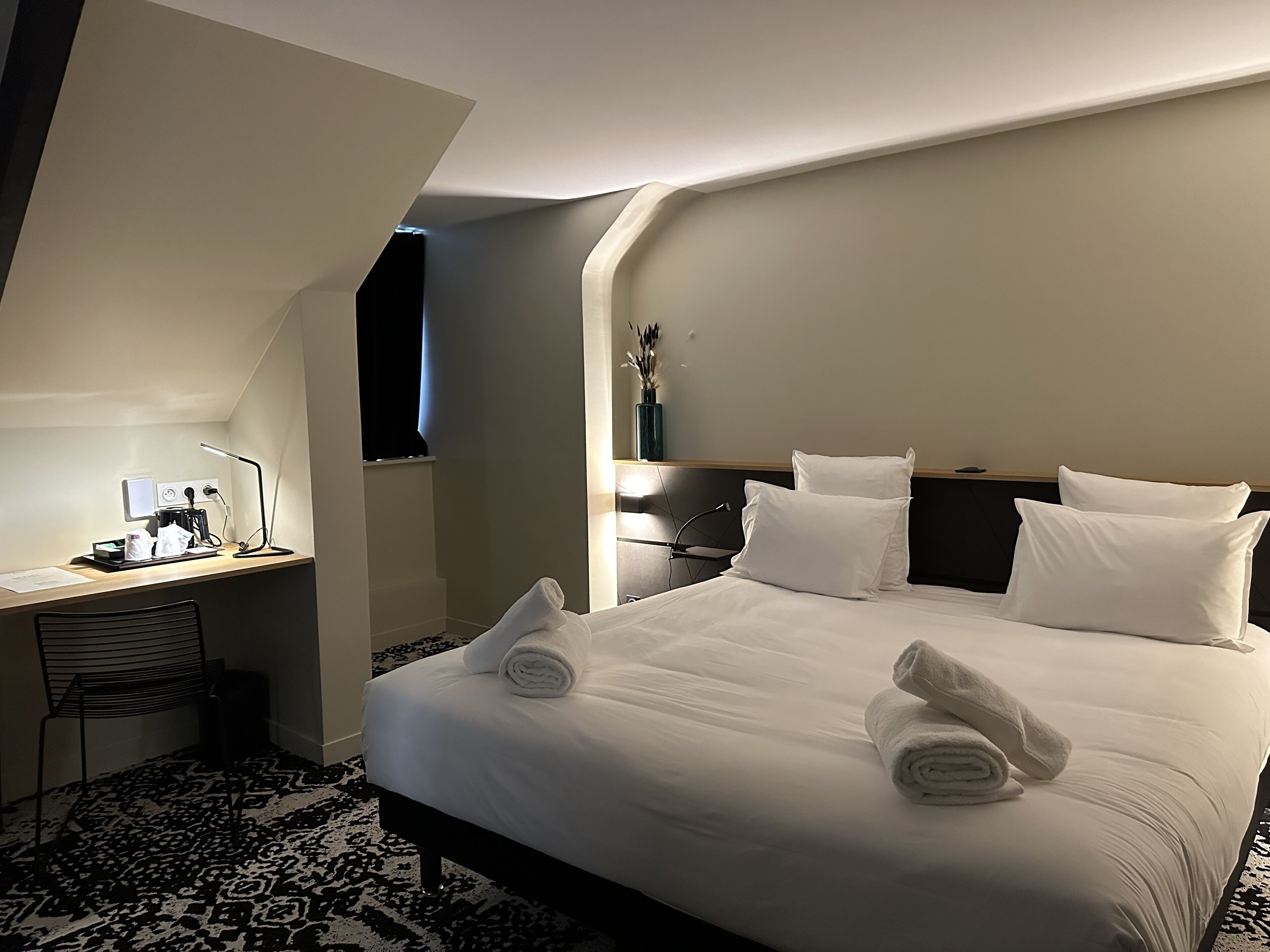 A hotel room with a large bed, a desk with a computer, and a chair.