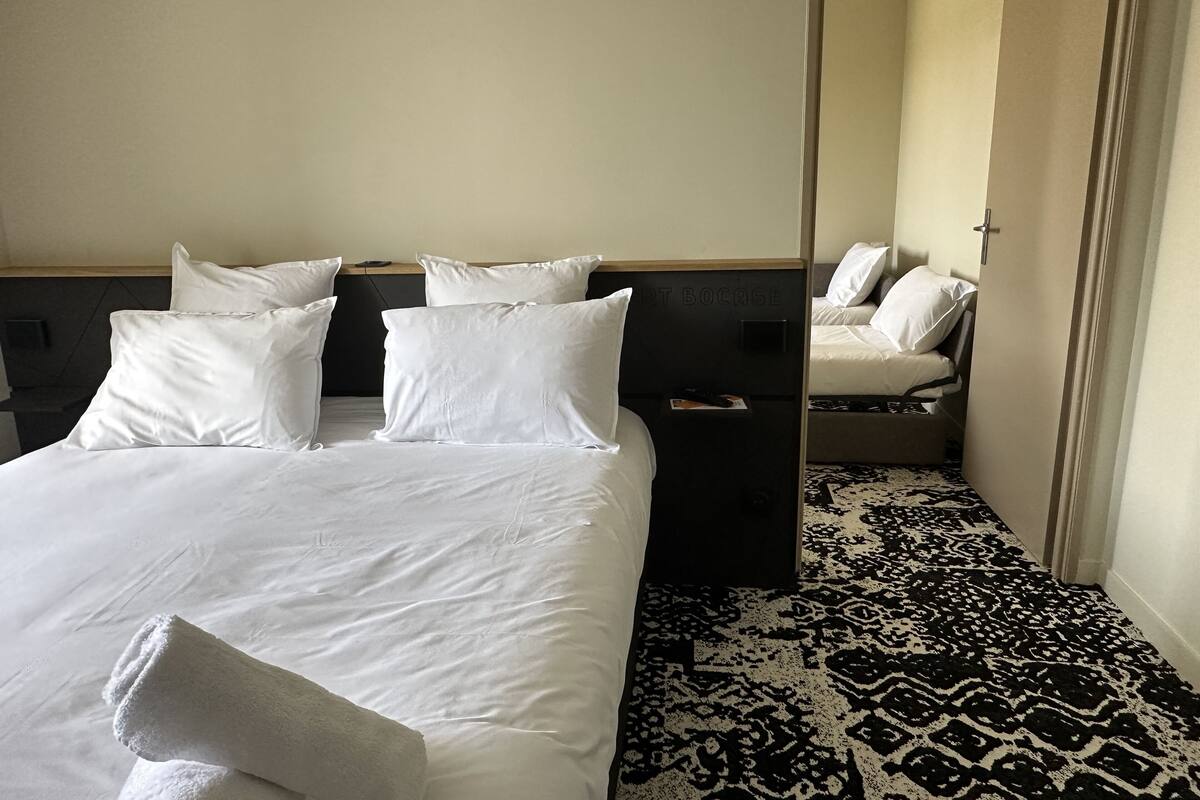 Hotellihuone, jossa on suuri sänky, useita tyynyjä, yöpöytä ja kuviollinen matto.