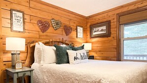 Een gezellige slaapkamer met een houten hoofdbord, een groot bed met een witte deken, twee bedlampjes en decoratieve hartvormige wanddecoratie.