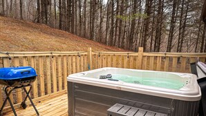 Un jacuzzi en una terraza de madera, con un cerco de madera y árboles al fondo.