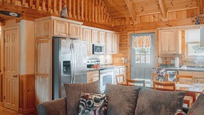 Ein gemütliches Blockhaus-Interieur mit Holzwänden und -decken, einem Essbereich mit Tisch und Stühlen sowie einer Küche mit Geräten.
