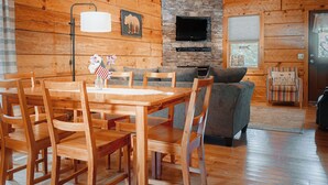 Ein gemütliches Blockhauss-Interieur mit Essbereich, Kamin, Fernseher und einer Couch.
