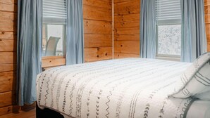 Ein Zimmer in einer Holzhütte mit einem Bett, zwei Vorhängen und Blick ins Freie.