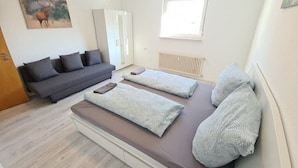 Una habitación con sofá, dos mesas de masaje con toallas, un radiador y una puerta.