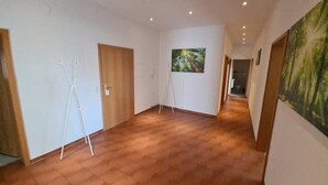 Un pasillo con suelo de madera, paredes blancas y un cuadro enmarcado a la derecha.