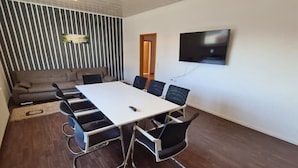 Una sala de conferencias con una mesa blanca, sillas negras, un sofá y un televisor instalado en la pared.
