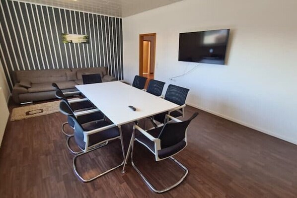 A conference room with a white table, black chairs, a sofa, and a TV mounted on the wall. - Großzügiger Wohntraum - nur 10 min zu Fuß vom Europapark! (Rust)