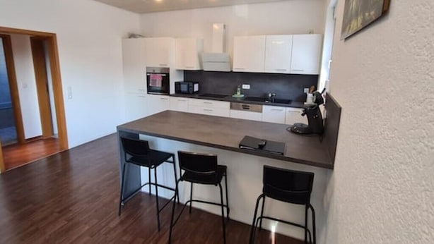 Una cocina moderna con armarios blancos, una isla central con taburetes y un microondas.