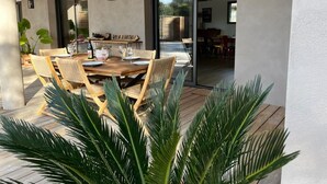 An outdoor dining area with a wooden table and wicker chairs, a glass door leading to a covered patio, and a sign that reads "Villa Natas." - Special vacation villa  (San-Gavino-Di-Carbini)