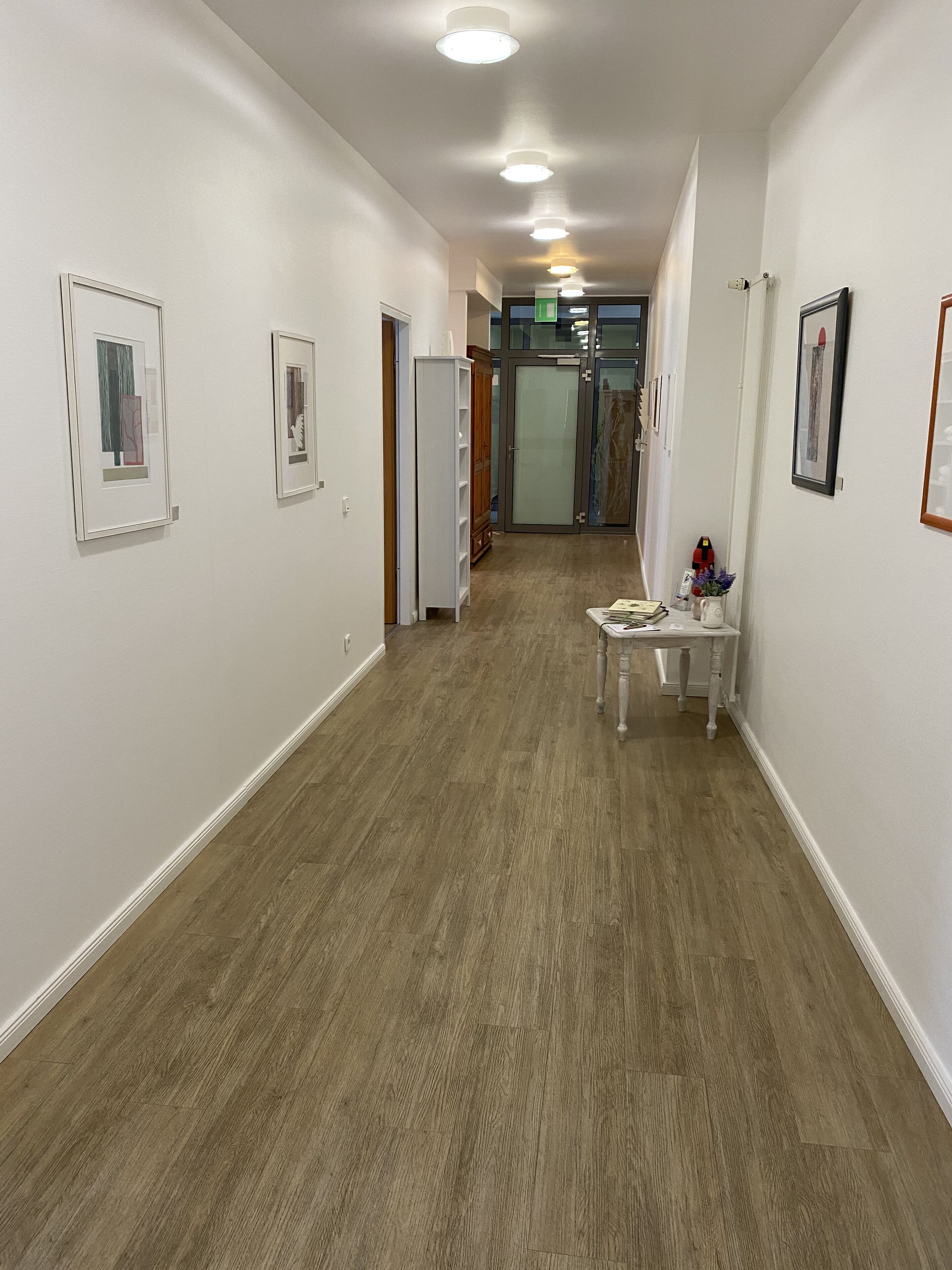 A hallway with wooden flooring, white walls, and framed artwork.