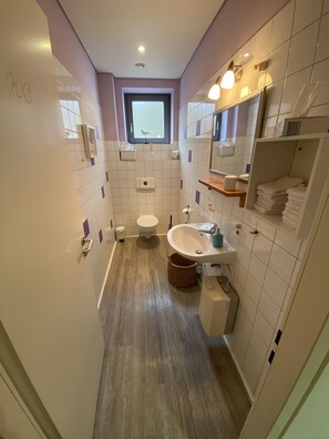 Un baño moderno con inodoro, lavamanos y bañera. Hay una ventana sobre el inodoro y un estante con toallas.