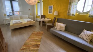 A room with a bed, a sofa, a dining table, and a hanging light fixture. - Gästehaus Lavendel (Flensburg)