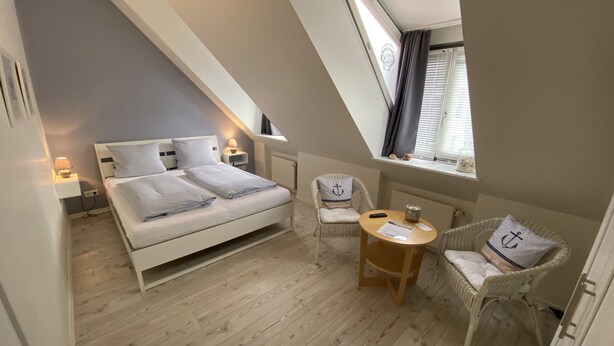 A bedroom with a bed, two chairs, a small table, and a window with curtains. - Gästehaus Lavendel (Flensburg)