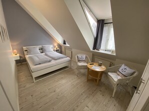 Un dormitorio con una cama, dos sillones, una mesita y una ventana con cortinas.
