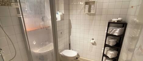 A modern bathroom with a glass-enclosed shower, a toilet, and a shelf with towels.