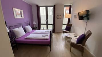 Una habitación con cama, una silla, una mesa, un televisor y una ventana.